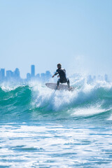 Naklejka premium Professional surfer in black wetsuit riding a wave on the city beach