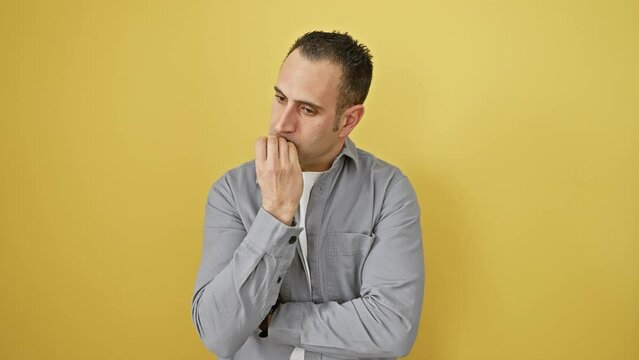 Young hispanic man wearing shirt standing looking stressed and nervous with hands on mouth biting nails. anxiety problem. over isolated yellow background
