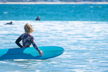 Blonde woman with floral swimsuit entering the sea water with her surfboard