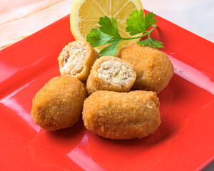 Fried croquettes served with a lemon wedge and parsley on a red plate, typical food, typical mediterranean mallorcan cuisine typical from balearic islands mallorca, spain