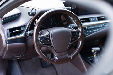 Car steering wheel. Brown leather dashboard, climate control, speedometer, display, wood decoration. Expensive car interior with steering wheel.