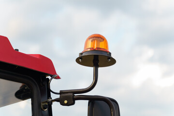 Orange Beacon Light on Farm Tractor Against Cloudy Sky © Dzmitry