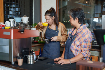 Asian daughter of business owner of  small cafe single mother retired pensioner Learning to make coffee  taste coffee yellow coffee cup There coffee maker Mom standing there teaching  make coffee
