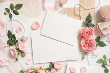 Fototapeta na wymiar Blank cards near pink roses, engagement ring and silk ribbons top view, wedding mockup