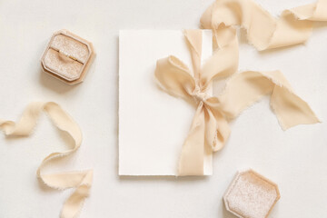 Card tied with a beige silk ribbons near engagement ring on white table top view, mockup