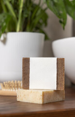 Soap bar with blank label on bath wooden countertop near monstera plant close up, mockup