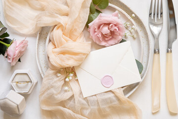 Envelope near cream fabric knot and light pink roses on plates top view copy space, wedding mockup