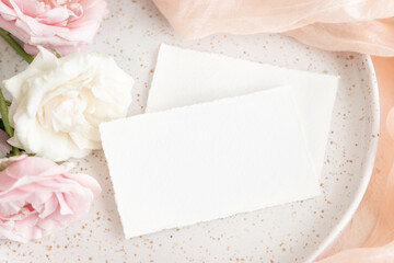 Cards near light pink tulle fabric and roses on plate top view copy space, wedding mockup