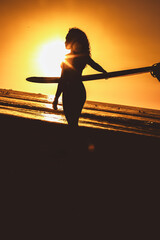 Sunset silhouette of a woman holding a surfboard