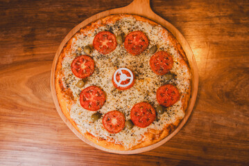 Overhead view of a Neapolitan pizza on a tray on a wooden table. - Powered by Adobe