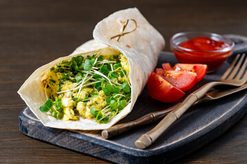 Homemade burrito wraps with scrambled egg omelet and microgreens for healthy breakfast on wooden board, closeup