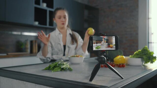 Young woman video lesson about cooking. Positive girl talks recording video lesson, filming cooks tutorial in modern kitchen studio. Concept for online healthy cooking courses, recording of training.
