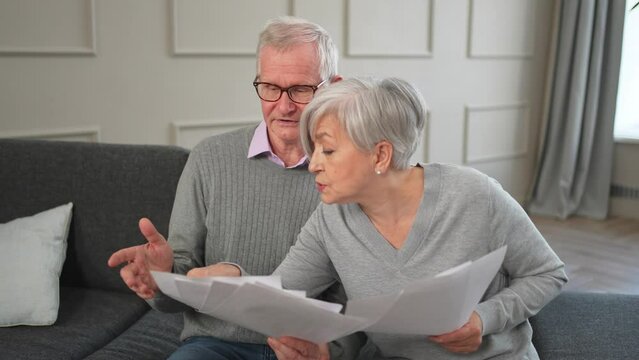 Sad tired disappointed middle aged senior couple sit with paper document. Unhappy older mature man woman reading paper bill managing bank finances calculating taxes planning loan debt pension payment