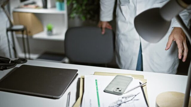 Focused man in white lab coat with stethoscope at medical office desk with laptop and documents