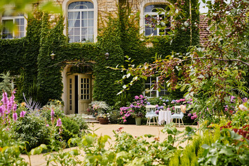 object photo of beautiful cottage house with table and chairs in front of it, full of plants