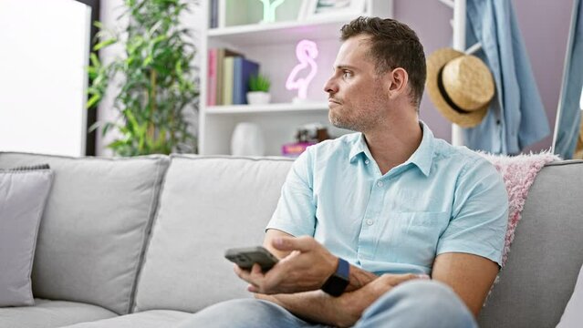 Handsome man with beard using smartphone on couch in modern living room interior