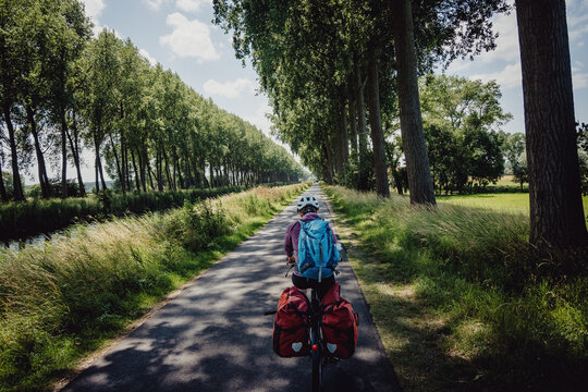 Frau radelt w&auml;hrend einer Radreise auf einem Radweg entlang eines Kanals in Flandern, Belgien