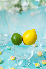 grüne Limette und gelbe Zitrone als Einheit auf Glas mit Bonbons auf Tisch mit blauem Grund und...