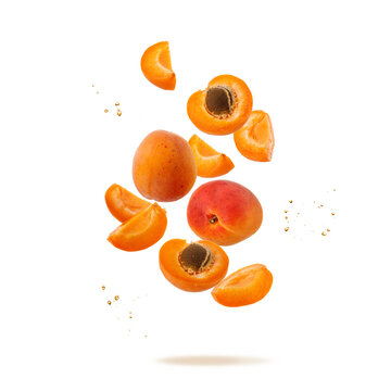 Fresh ripe whole and sliced apricot fruits with juice drops flying falling isolated on white background.