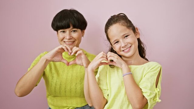 Confident mother, daughter make heart gesture with hands, smiling over isolated pink background in a symbol of love, happiness and family bond.