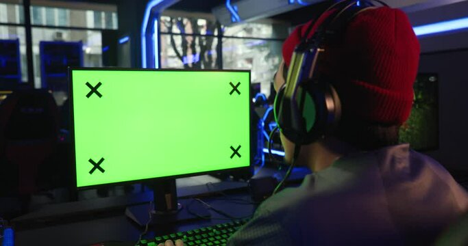 Male gamer playing video games with a green screen monitor in a gaming room