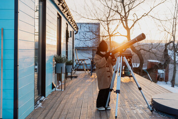 Cute little Girl with astronomical telescope stargazing under sunny sky.