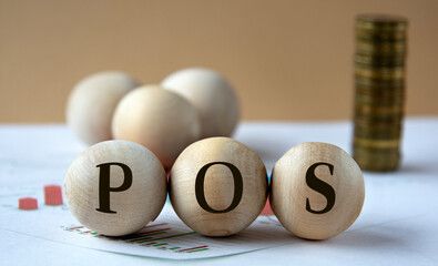POS - abbreviation on wooden balls on a background of coins and graphics.