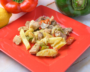 Pork with bell peppers and potatoes on a bright red plate, typical food, typical mediterranean mallorcan cuisine typical from balearic islands mallorca, spain