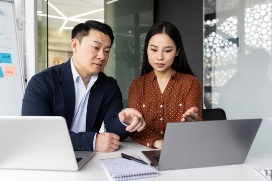 Two focused business colleagues working together on a laptop, engaged in a project discussion inside a modern office.