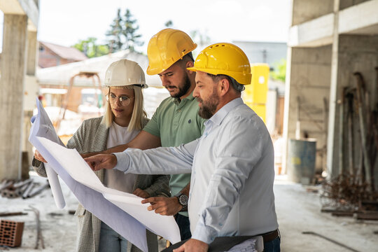 A group of architects  work together on-site, discussing blueprints and coordinating to bring their project to life.	