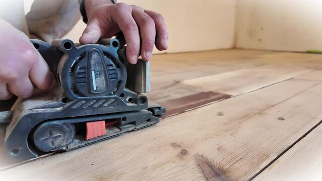 Repair work on a wooden floor using a sanding machine. Apartment renovation. Electric grinding floor polishing machine. A carpenter makes a parquet floor by sanding. Horizontal video.