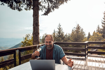 Man having a virtual toast during video call in a home with forest in the background