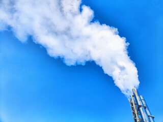 Air pollution by smoke coming out of factory chimney. White clouds of smoke against a blue sky background