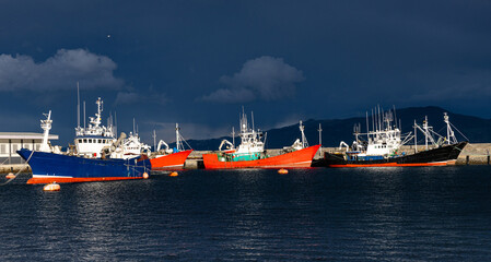 Fishing boats moored at harbor against stormy sky.