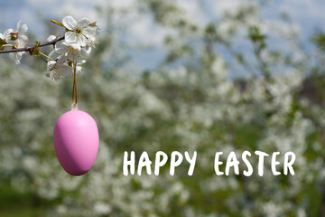 Greeting card with wishes of Happy Easter. Close-up of decorative Easter egg on branch against background of flowering trees. Holiday concept. Religious holiday of Easter. Nature. Springtime