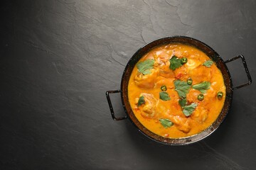Tasty chicken curry with parsley and pepper on black textured table, top view. Space for text