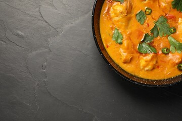 Tasty chicken curry with parsley and pepper on black textured table, top view. Space for text
