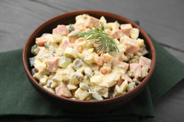 Tasty Olivier salad with boiled sausage in bowl on grey table, closeup