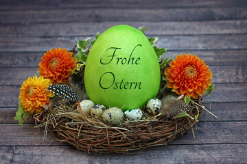 Grußkarte Frohe Ostern: Osterdekoration mit Ostereiern in einem Nest davon eins mit dem Text Frohe...