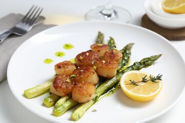 Delicious fried scallops with asparagus, lemon and thyme served on white table, closeup