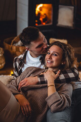 Beautiful young loving couple relaxing near fireplace in bed at home. Happy spouses enjoying lazy romantic winter cozy morning in bedroom. Candles, garlands, countryside interior. Romantic date