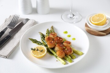 Delicious fried scallops with asparagus, lemon and thyme served on white table