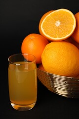 Bowl with ripe oranges and fresh juice on black background