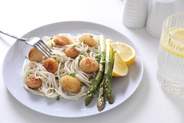 Delicious scallop pasta with asparagus, green onion and lemon served on white table, closeup