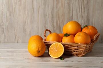 Many whole and cut oranges on light wooden table, space for text