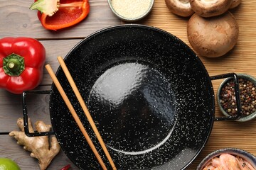 Black wok, chopsticks and products on color wooden table, flat lay