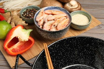 Black wok, chopsticks and bamboo mat with products on color wooden table, closeup