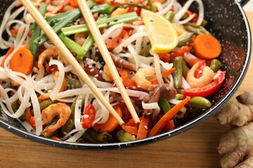 Shrimp stir fry with noodles and vegetables in wok on wooden table, closeup