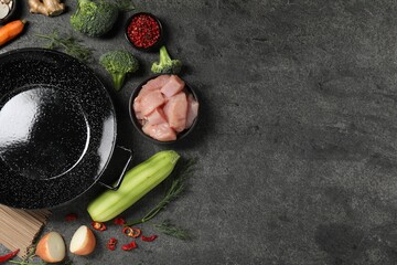 Empty iron wok surrounded by ingredients on grey table, flat lay. Space for text