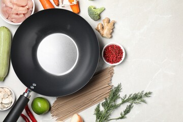 Empty iron wok surrounded by raw ingredients on light table, flat lay. Space for text